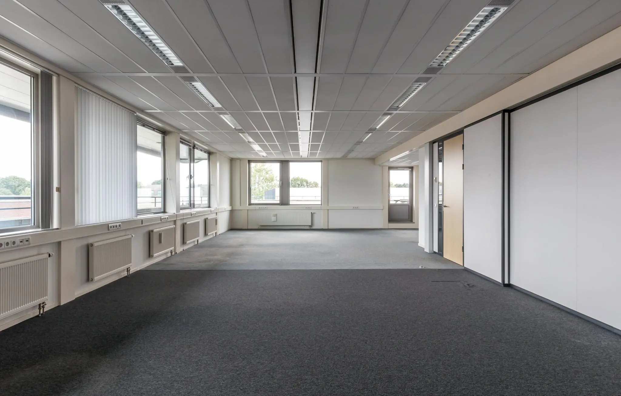 Leegstaand kantoorruimte in gebouw De Wel met grote ramen en systeemplafond.